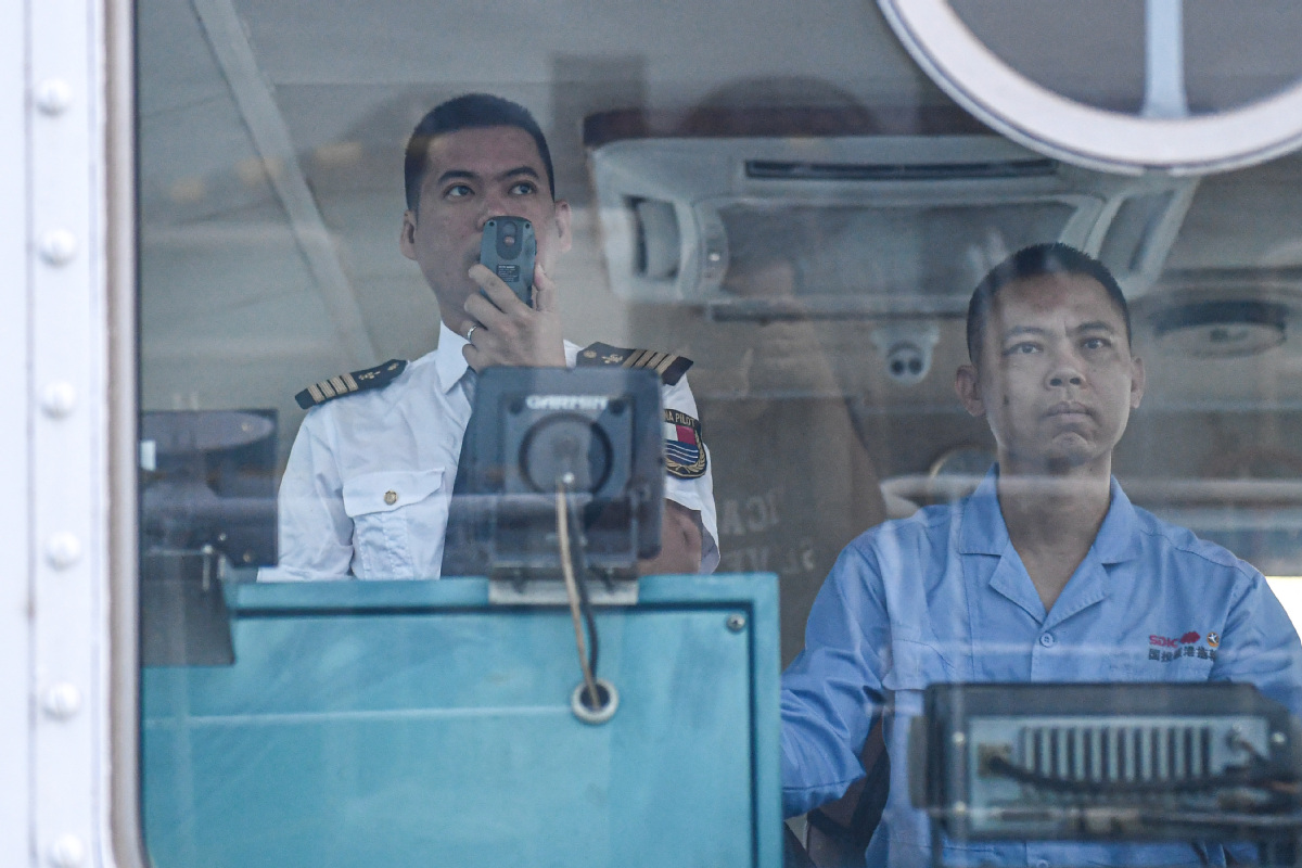 Lin Hongpin (left) uses a walkie-talkie to communicate with the ship he is about to pilot. [Photo by Pu Xiaoxu/Xinhua]
